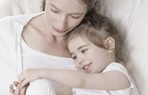 Mama in otrok ležita tesno skupaj in se objemata.
