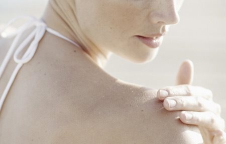 Ženska nanaša kremo na desno ramo.